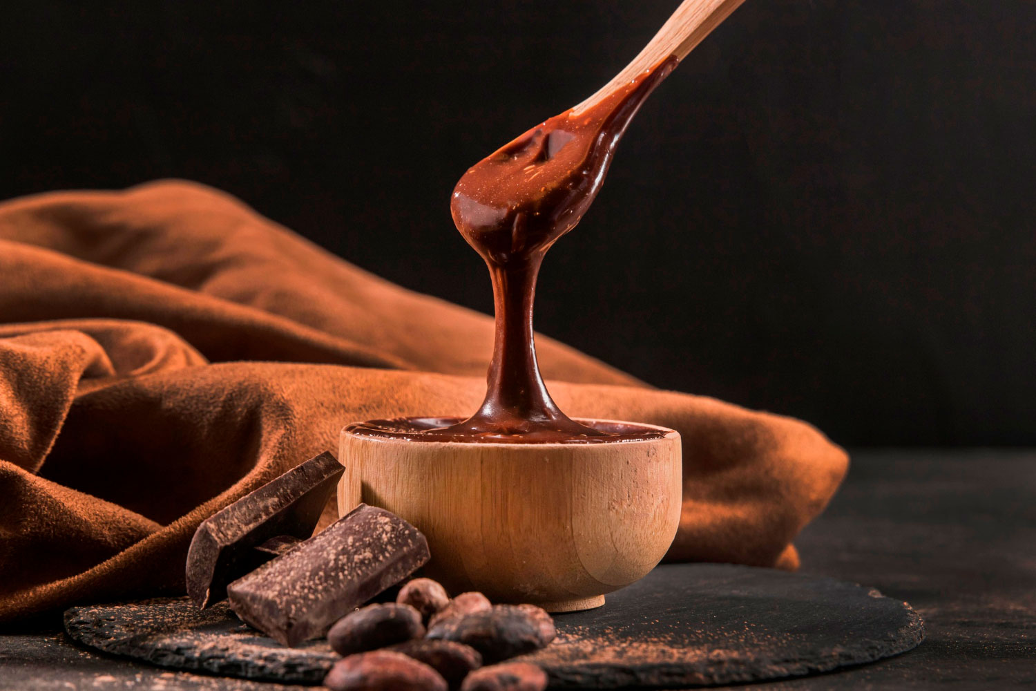 Vasilha com chocolate derretido com chocolate em barra e sementes de cacau ao lado representando visita à fábrica Nugali.